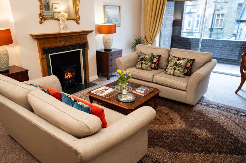 The sitting room in one of our apartments. Seasonal flowers are in a vase on the coffee table and the fire is on.